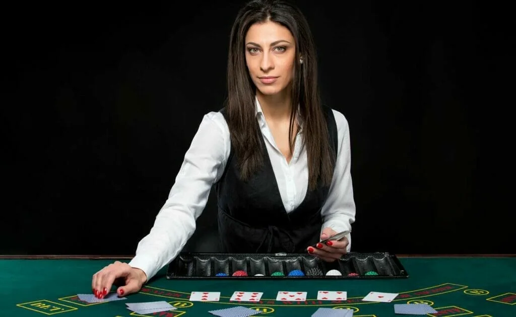 Dealer di meja kasino live dengan nuansa ruang permainan langsung